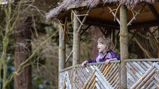 Plentyn yn crwydro'r Ardd Gorsiog o'r caban to gwellt yng Nghastell a Gardd Penrhyn, Cymru